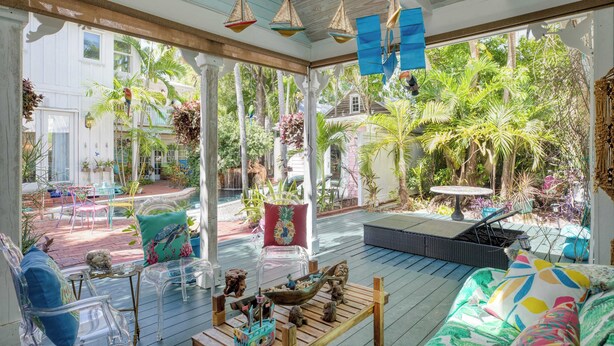 A spacious outdoor patio with clear glass furniture, a wooden table, and a variety of tropical plants. - Boat House by Avantstay Character Cottage Central Location w/ Shared Pool Month Long Stays (Key West)