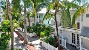 A multi-story building with white railings and balconies, surrounded by lush greenery and palm trees. - Breezy Bungalow by Avantstay Close 2 Zachary Taylor State Park w/ Shared Pool Month-long Stays (Key West)