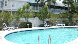 A swimming pool with lounge chairs, surrounded by a white fence and palm trees. - Breezy Bungalow by Avantstay Close 2 Zachary Taylor State Park w/ Shared Pool Month-long Stays (Key West)