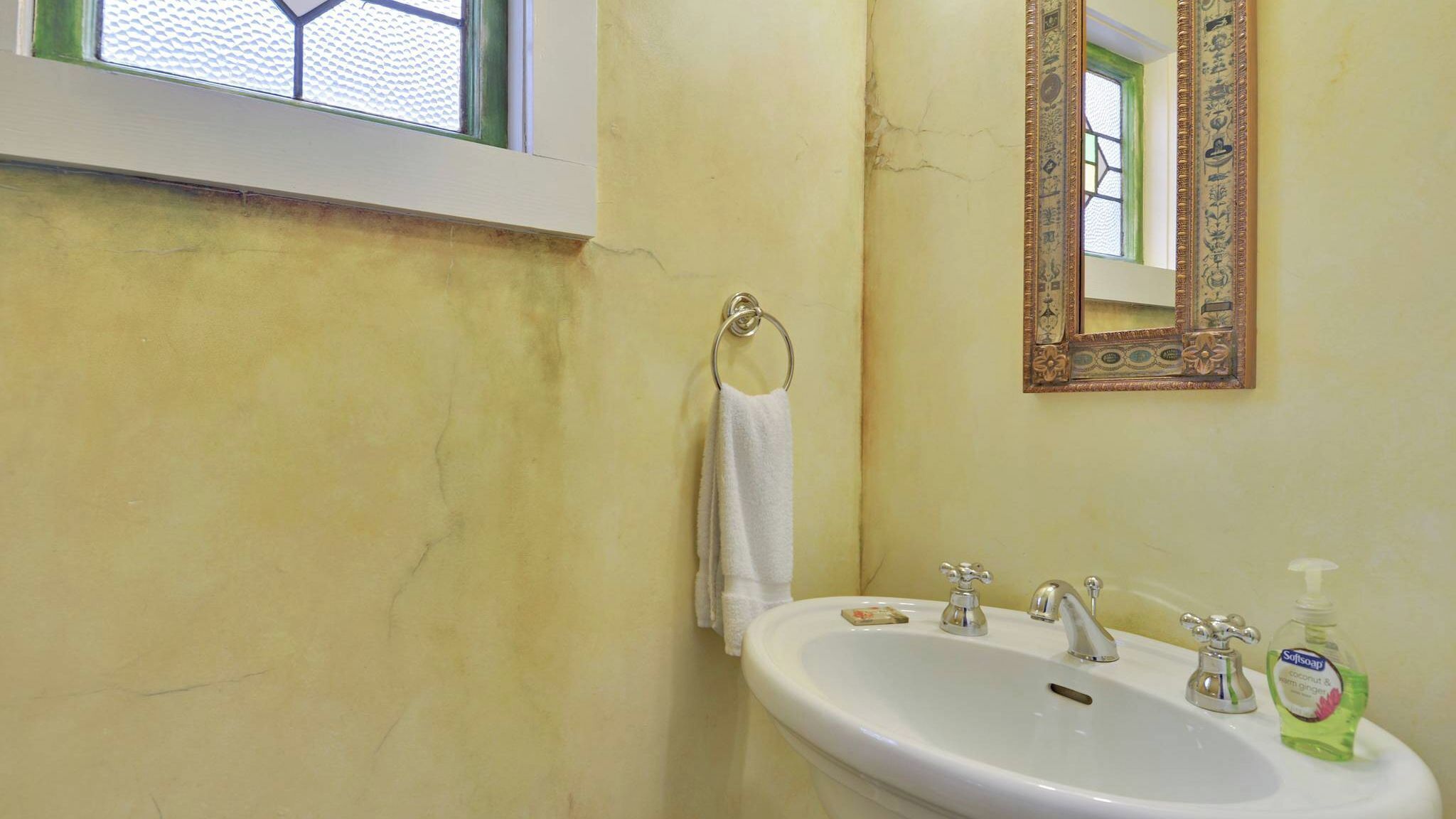 Une salle de bain avec un lavabo blanc, un miroir et une fenêtre dotée d’un cadre vert.