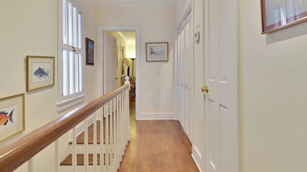 A hallway with a wooden staircase, white doors, and framed pictures on the walls. - Amelia Home by Avantstay In Historic Old Town w/ Pool (Key West)