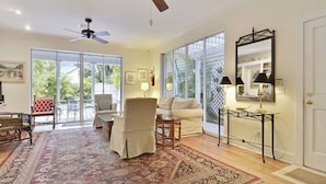 A spacious living room with a large window, a ceiling fan, a sofa, a coffee table, and a side table with lamps. - Amelia Home by Avantstay In Historic Old Town w/ Pool (Key West)