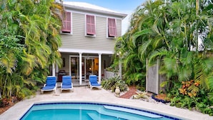A house with a swimming pool, two blue lounge chairs, and lush tropical plants. - Amelia Home by Avantstay In Historic Old Town w/ Pool (Key West)
