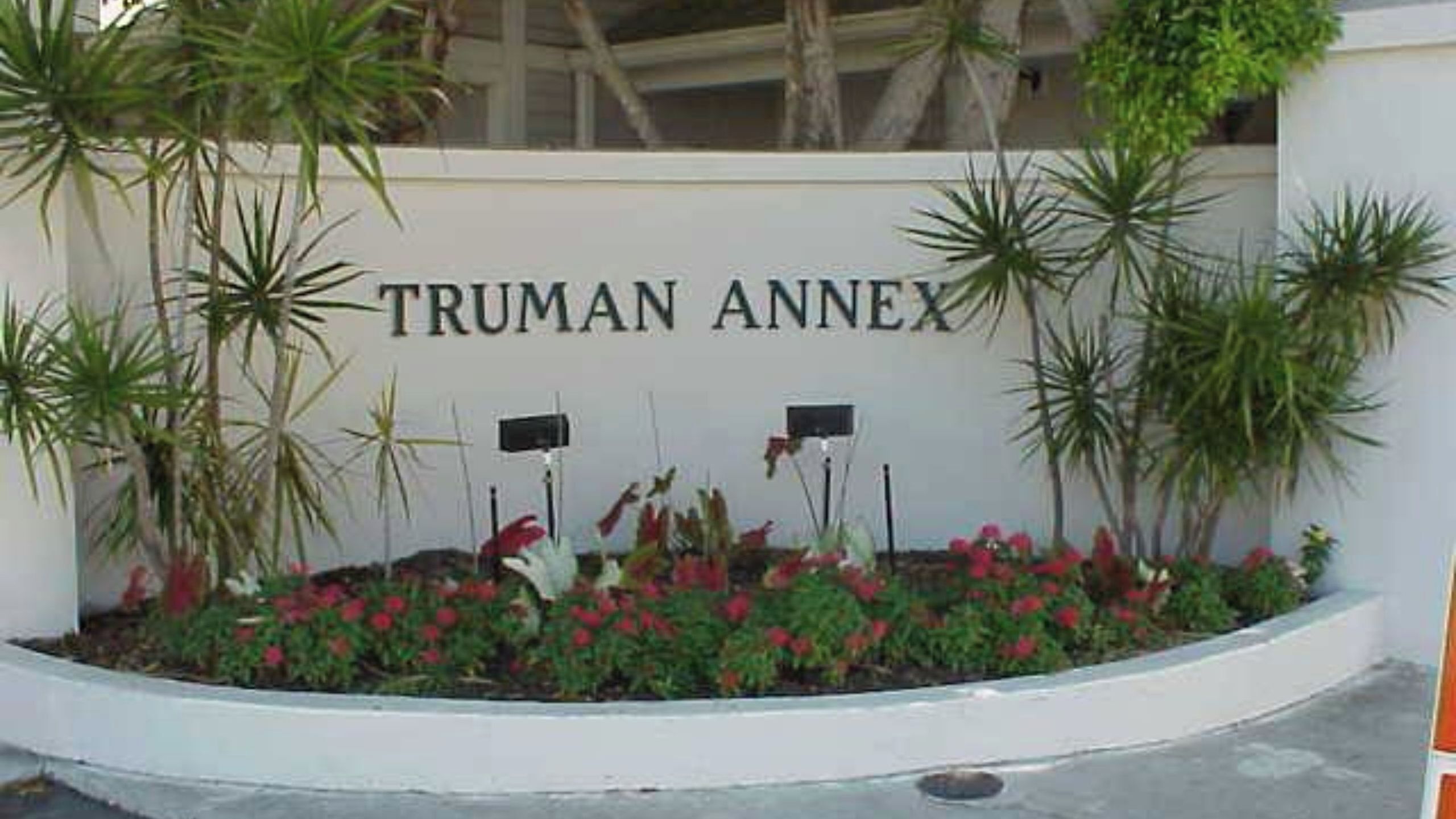 Ein Schild mit der Aufschrift 'TRUMAN ANNEX', umgeben von einer gepflegten Grünfläche mit verschiedenen Pflanzen und Büschen.