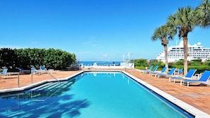 A swimming pool with lounge chairs, a palm tree, and a cruise ship in the background.