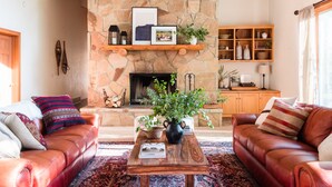 A cozy living room with leather sofas, a stone fireplace, a wooden coffee table, and a bookshelf.