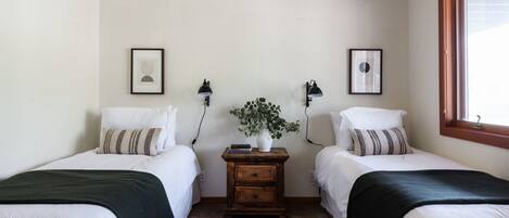 A room with two single beds, a nightstand with a plant, and framed pictures on the walls.