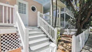 Une maison à deux étages avec un porche blanc à l’avant, un escalier en bois et une plaque portant le numéro « 69 ».