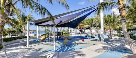 A playground with a swing set, slides, and a shaded area under a canopy.