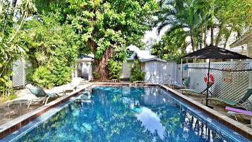 A swimming pool surrounded by lush greenery and a fenced area with lounge chairs.