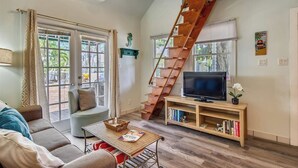 Un salon avec un escalier en bois, un canapé, un téléviseur posé sur un meuble en bois et une bibliothèque.