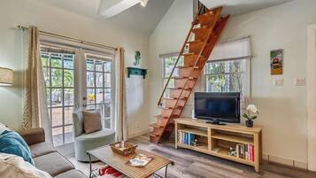 A living room with a wooden staircase, a sofa, a TV on a wooden stand, and a bookshelf.