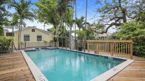A swimming pool with a wooden deck, surrounded by palm trees and a house. - Land Of Love by Avantstay Pets Allowed! Shared Pool! Great Location! Month Long Stays Only (Key West)