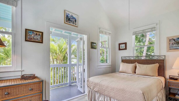 Un dormitorio con una cama grande, un aparador y un balcón con vistas a palmeras.