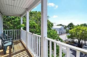 A wooden deck with white railings, a covered area, and a view of a street with parked cars and trees. - Duval Breeze by Avantstay Great Location Close to Beach & Nightlife Shared Pool! Week Long Stays (Key West)