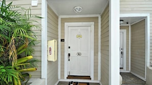 A white door with a number plate, a welcome sign, and a doormat with shoes.