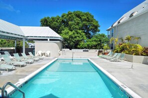 A rectangular swimming pool with a white deck, surrounded by lounge chairs and a covered seating area. - Duval Breeze by Avantstay Great Location Close to Beach & Nightlife Shared Pool! Week Long Stays (Key West)