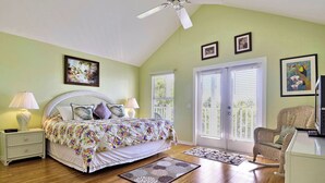 A bedroom with a bed, nightstands, a chair, a ceiling fan, and two windows with blinds.