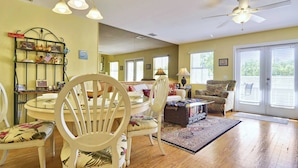 A living room with a dining table, chairs, a sofa, a ceiling fan, and a large mirror.