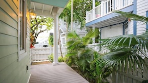 A wooden deck with a white fence, a covered porch, and lush green plants. - Ecco Domani by Avantstay Gorgeous Home w/ Pool, Balcony in Great Location Month Long Stays Only (Key West)