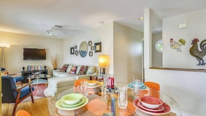 A living room with a sofa, a TV, a dining table set with plates and glasses, and a wall with decorative items. - Pool, 2 Blocks to Duval St, Gated Community Month Long Stays Shipyard Treasure by Avantstay (Key West)