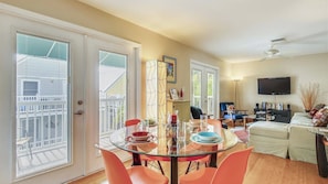 A dining area with a glass table and orange chairs, a living room with a sofa and TV, and a balcony with blinds. - Pool, 2 Blocks to Duval St, Gated Community Month Long Stays Shipyard Treasure by Avantstay (Key West)