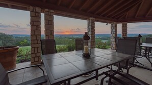 An outdoor patio with stone pillars, a table with chairs, and a view of the landscape. - 10,000 Sq.Ft Lux Estate on 650 Acres with Amazing Pool, Spa & Hill Country Views (Marble Falls)