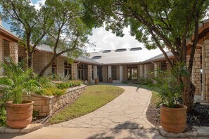 A courtyard with a stone pathway, potted plants, and a building with a flat roof.