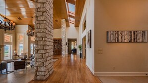 A spacious hallway with wooden flooring, stone pillars, and a skylight. - 10,000 Sq.Ft Lux Estate on 650 Acres with Amazing Pool, Spa & Hill Country Views (Marble Falls)