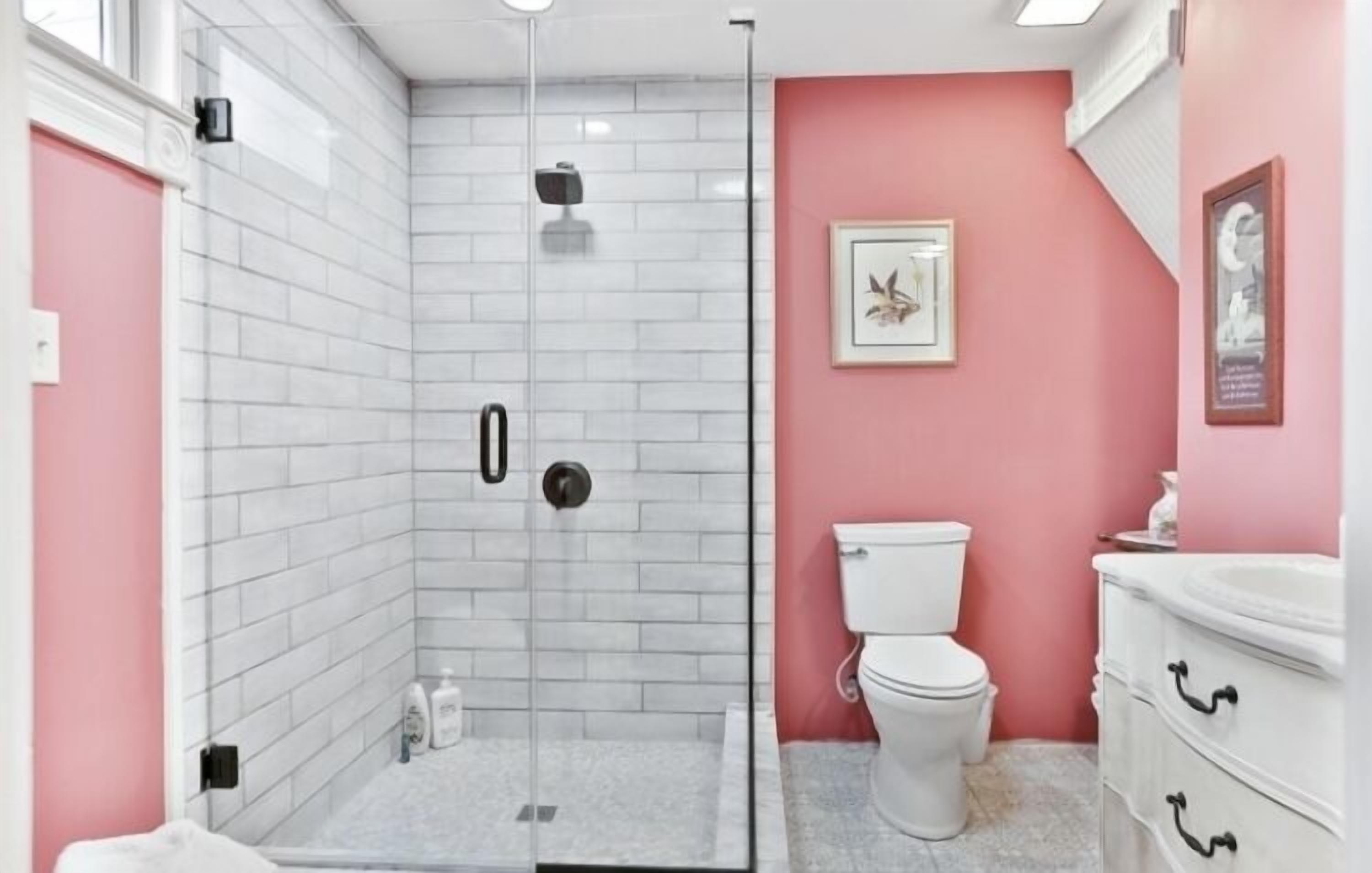 Un baño con ducha envuelta en vidrio, un inodoro blanco y una pared rosa.