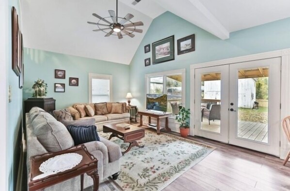 A living room with a sofa, coffee table, and a ceiling fan. There are framed pictures on the wall and a door leading outside. - Beautiful restored Victorian farmhouse (Shelbyville)