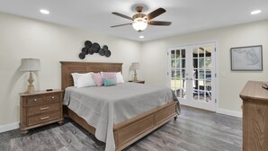 A bedroom with a wooden bed, two bedside tables, a ceiling fan, and a view to the outside. - Coastal Heated Pool Home, 10 mins to the beach and downtown  (St. Augustine)