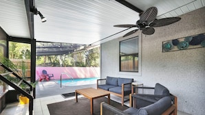 A covered outdoor seating area with a pool in the background, a ceiling fan, and a staircase leading to an upper level. - Coastal Heated Pool Home, 10 mins to the beach and downtown  (St. Augustine)