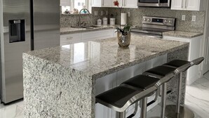 A modern kitchen with white cabinets, stainless steel appliances, granite countertops, and a central island with bar stools. - Beautiful home in Calusa, Key Largo (Key Largo)