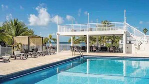 A swimming pool with lounge chairs and a covered area, surrounded by palm trees and a clear sky. - Beautiful home in Calusa, Key Largo (Key Largo)