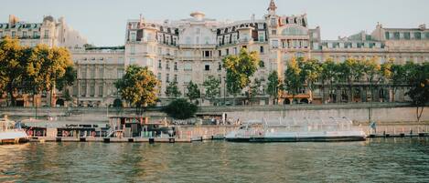 A waterfront hotel with a large building, a dock with boats, and a river.