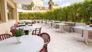 Un espace extérieur aménagé en terrasse, avec des tables et des chaises rondes, entouré d’une clôture en bambou.