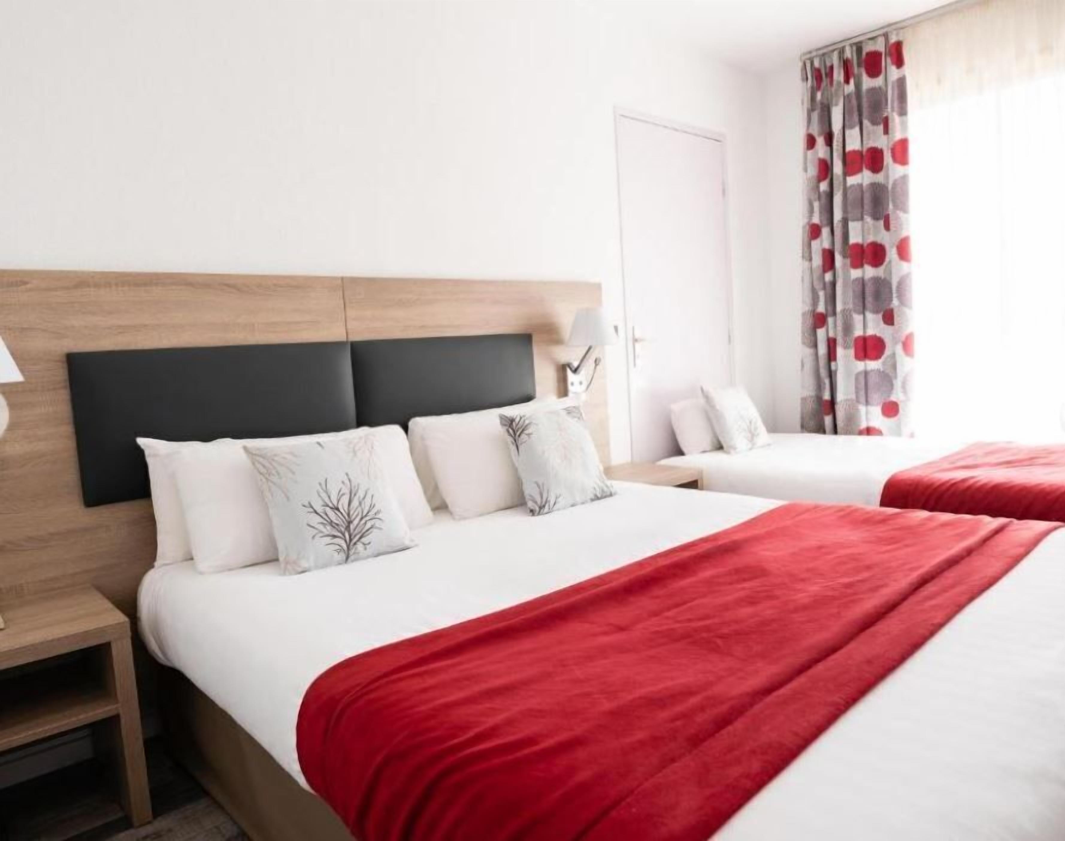 Habitación de hotel con dos camas, cabecero de madera, ropa de cama blanca y una manta roja.
