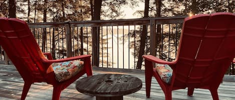 A wooden deck with two red Adirondack chairs and a round table.