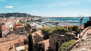 Un paisaje urbano costero con edificios históricos, un puerto deportivo lleno de barcos y un cielo azul despejado.