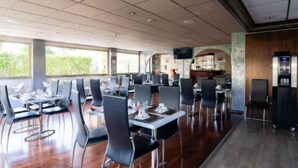 Un restaurante moderno con mesas y sillas altas, una zona de bar y grandes ventanales que ofrecen vistas al exterior.
