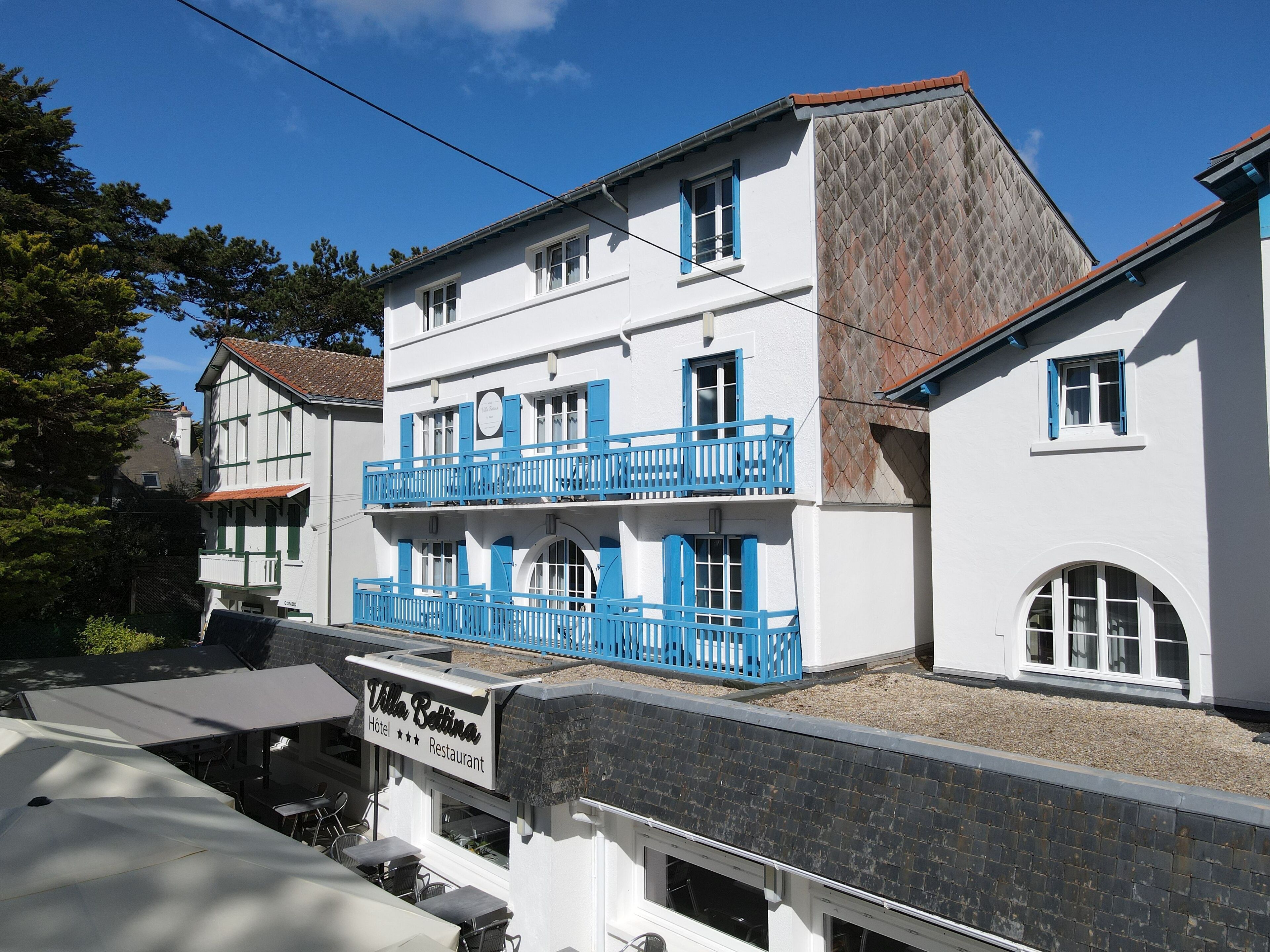 Een gebouw met twee verdiepingen, een balkon, een bord dat het een hotel en restaurant aangeeft, en een helderblauwe lucht op de achtergrond.
