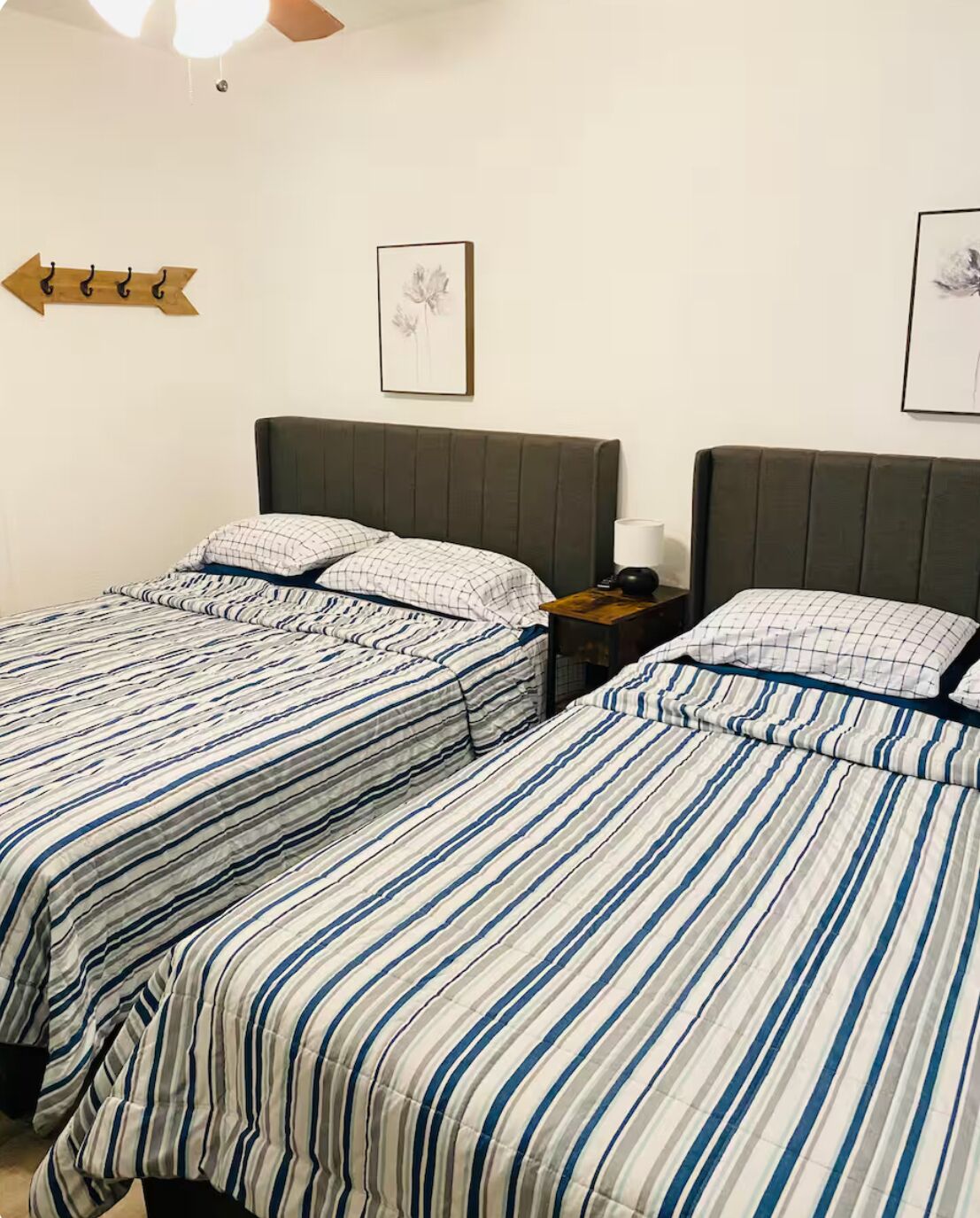 A hotel room with two beds, each with striped bedding, a nightstand with a lamp, and a framed picture on the wall.