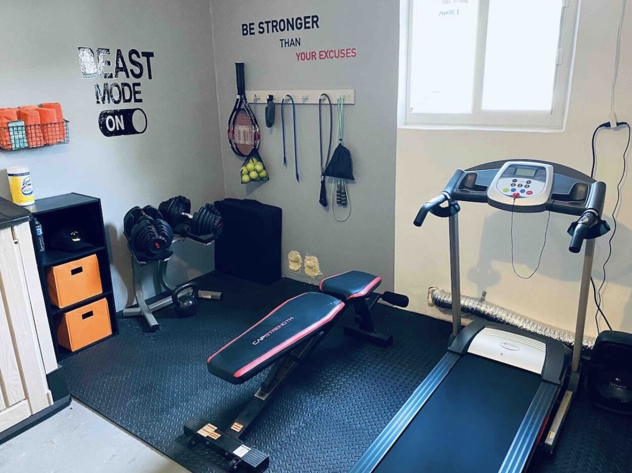A home gym with a treadmill, bench, and various exercise equipment.
