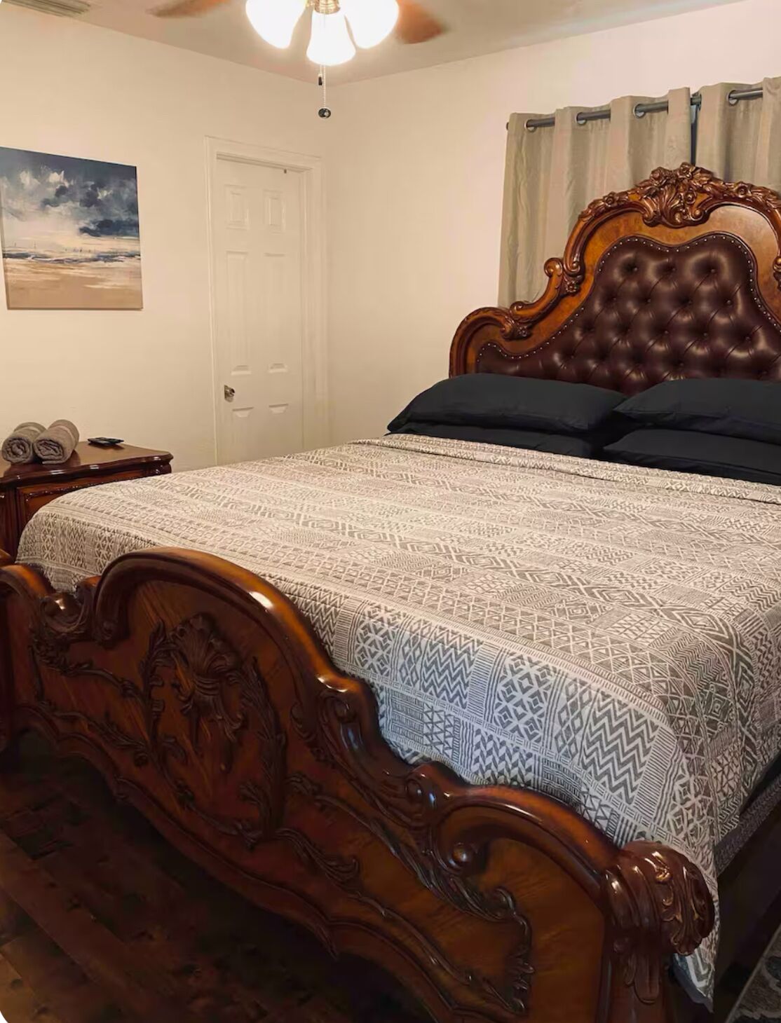 Un dormitorio con una cama de madera, un ventilador de techo, un cuadro en la pared y una puerta.