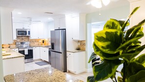 A modern kitchen with white cabinets, stainless steel appliances, granite countertops, and a ceiling fan. - Skyline Breeze - Minutes from downtown Jensen Beach (Jensen Beach)