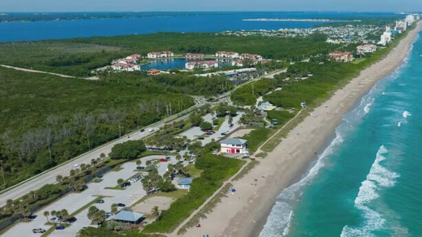An aerial view of a coastal area with a beach, a parking lot, and a cluster of buildings. - Skyline Breeze - Minutes from downtown Jensen Beach (Jensen Beach)