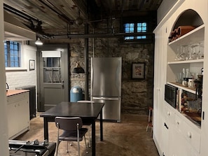 Una cocina con pared de piedra, refrigerador de acero inoxidable, mesa de madera y un lavamanos.