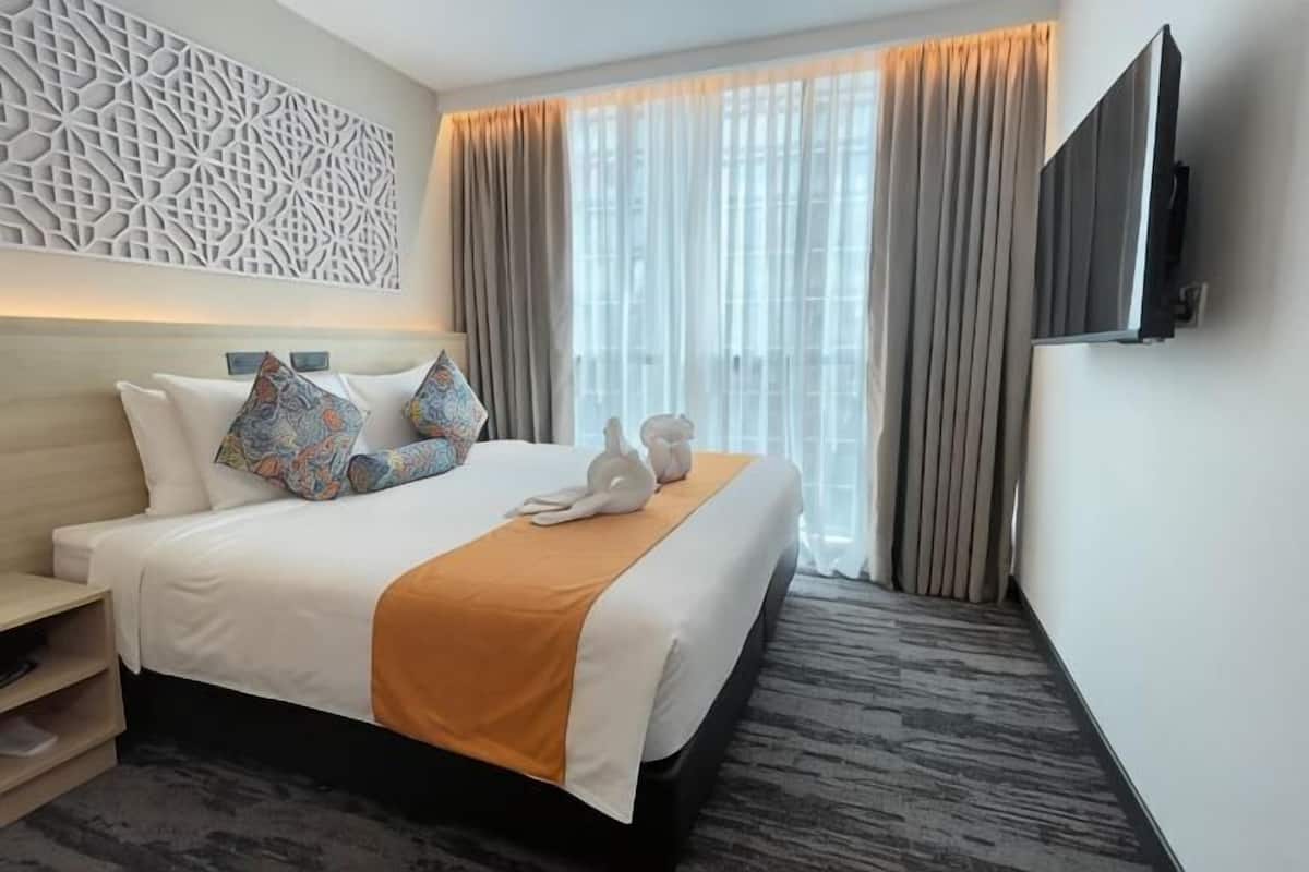 A hotel room with a large bed, a flat-screen TV, a decorative wall panel, and a window with curtains.