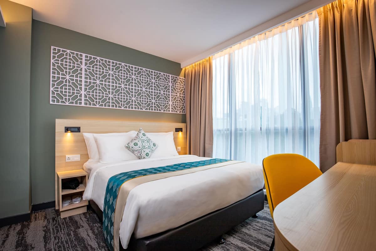 A hotel room with a bed, a nightstand, a chair, and a large window with curtains.